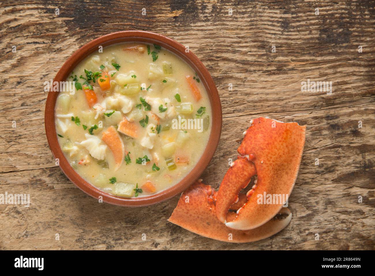 A lobster, Homarus gammarus, that has been caught in the English and homecooked in a chowder. Served in a bowl on a wooden board decorated with lobste Stock Photo