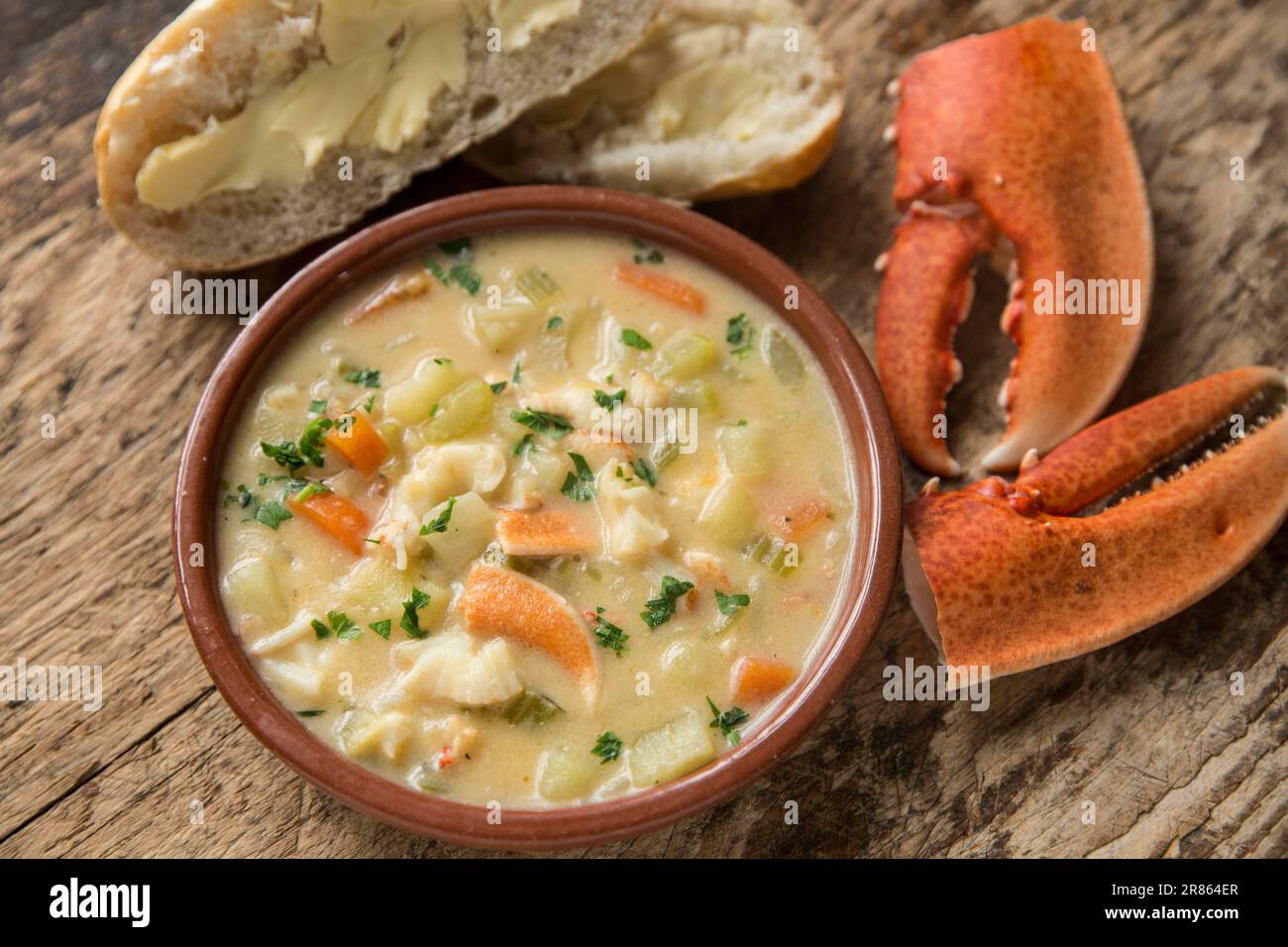 A lobster, Homarus gammarus, that has been caught in the English and homecooked in a chowder. Served in a bowl on a wooden board with buttered bread a Stock Photo