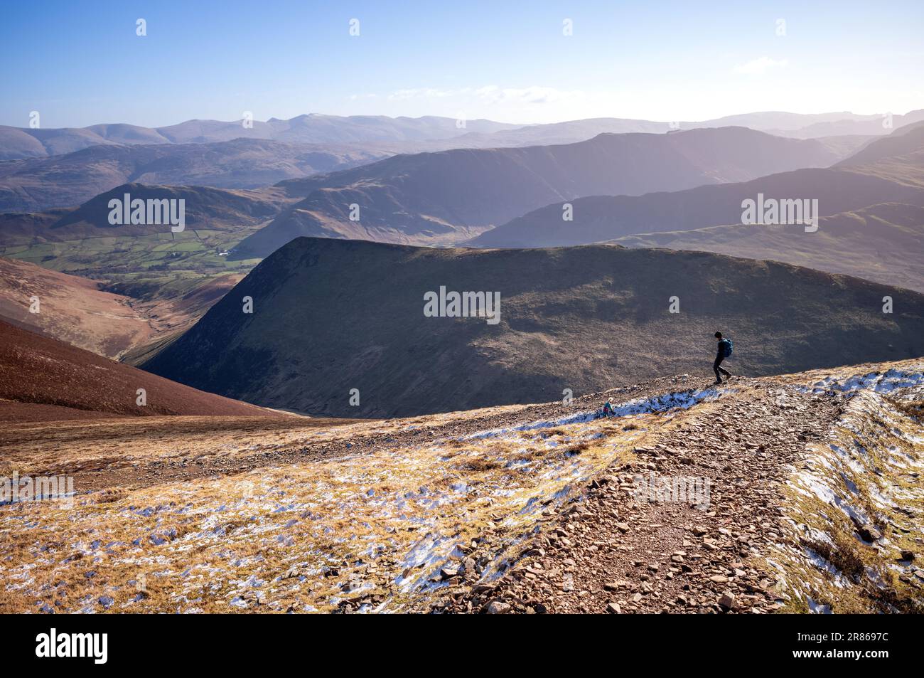 A female hiker and their dog descending a rocky trail from the summit of Sail towards Causey Pike with Ard Crags in the distance in winter in the Engl Stock Photo