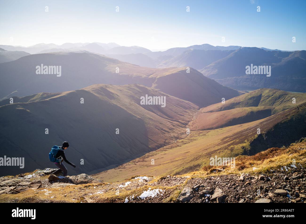 A female hiker descending a rocky path towards Sail from Crag Hill with the summits of High Snockrigg and Robinson in winter in the English Lake Distr Stock Photo