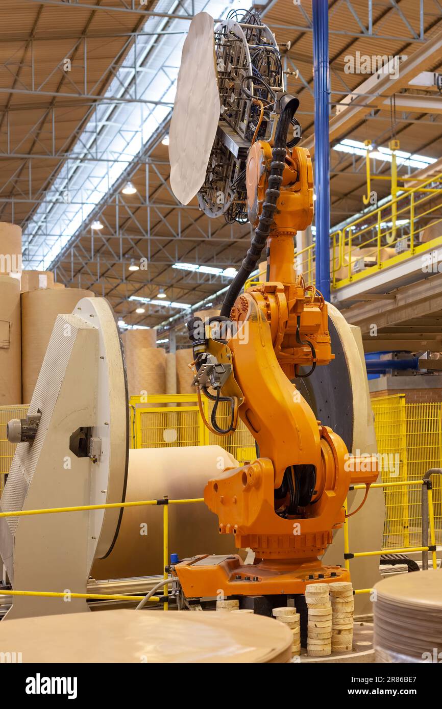 A robotic arm packaging large rolls of paper in a paper mill plant