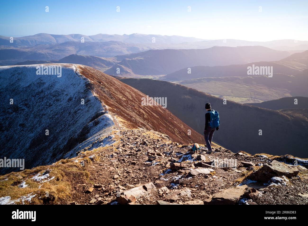 A female hiker and their dog walking down towards the summit of Sail from Crag Hill in winter in the English Lake District, UK. Stock Photo