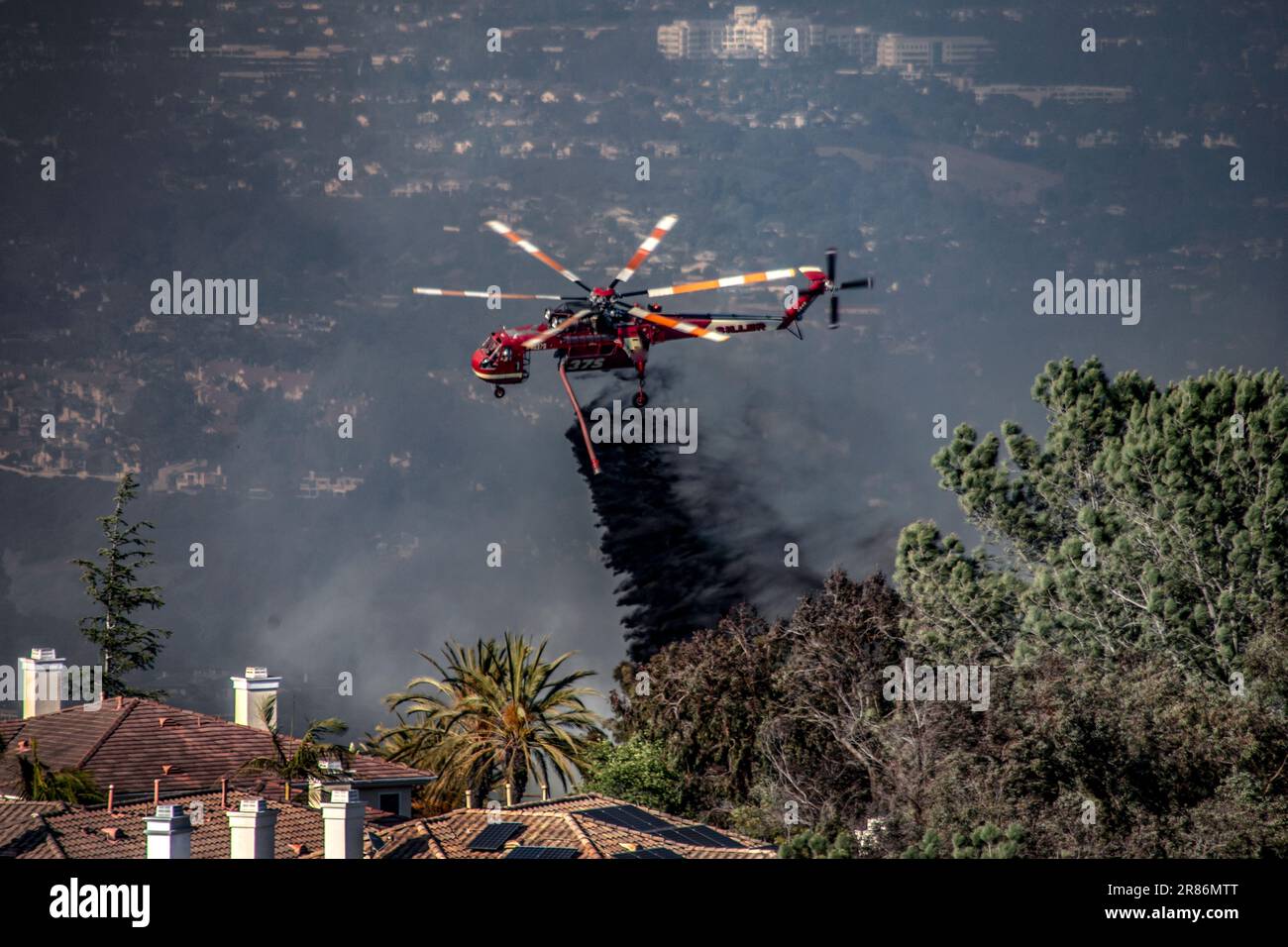 A fire fighting helicopter drops fire retardant on a blaze at a suburban residential community in Laguna Niguel, CA. Note smoky sky. Stock Photo