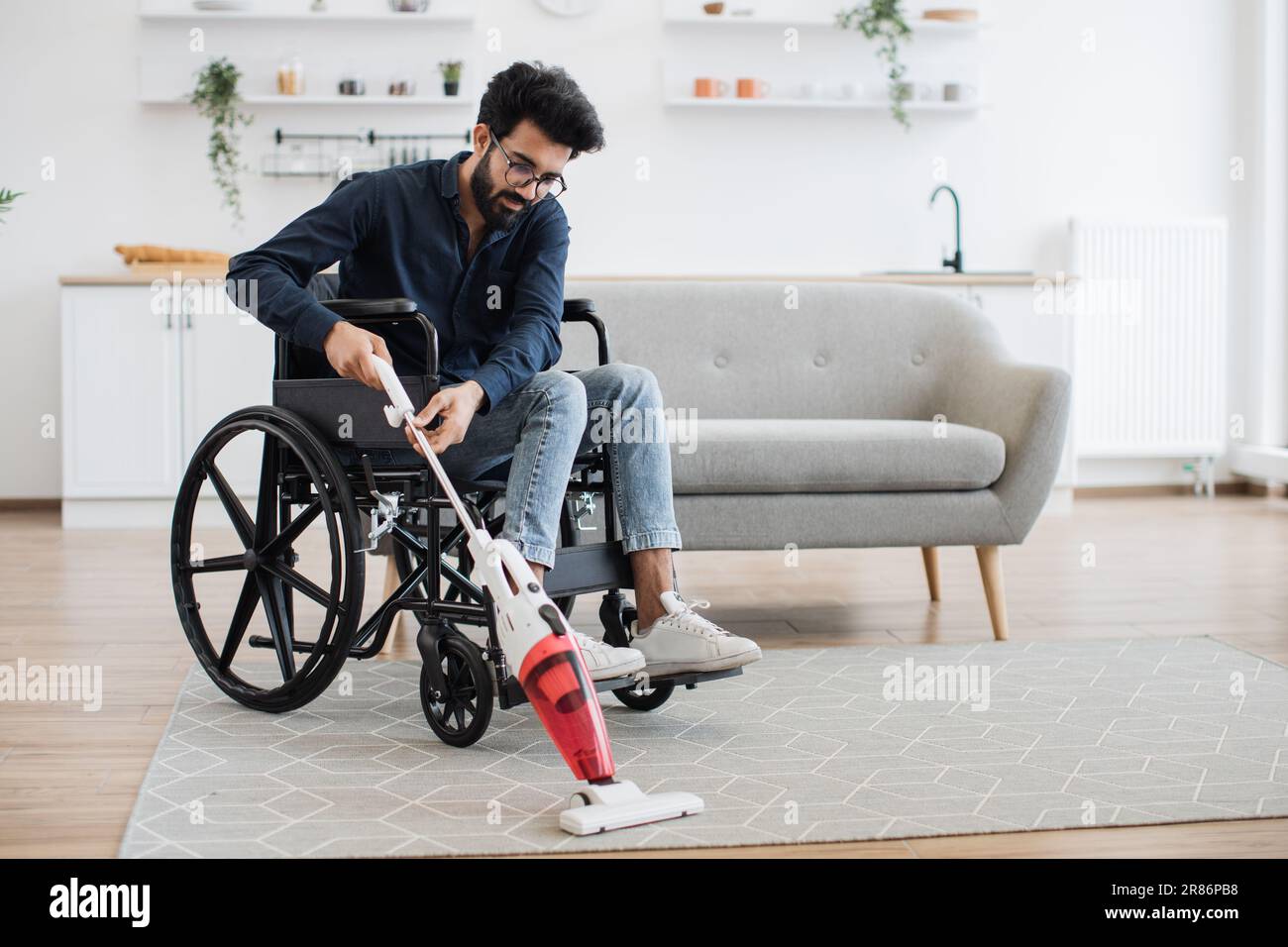 Helpful young man with disability holding cordless vacuum cleaner while