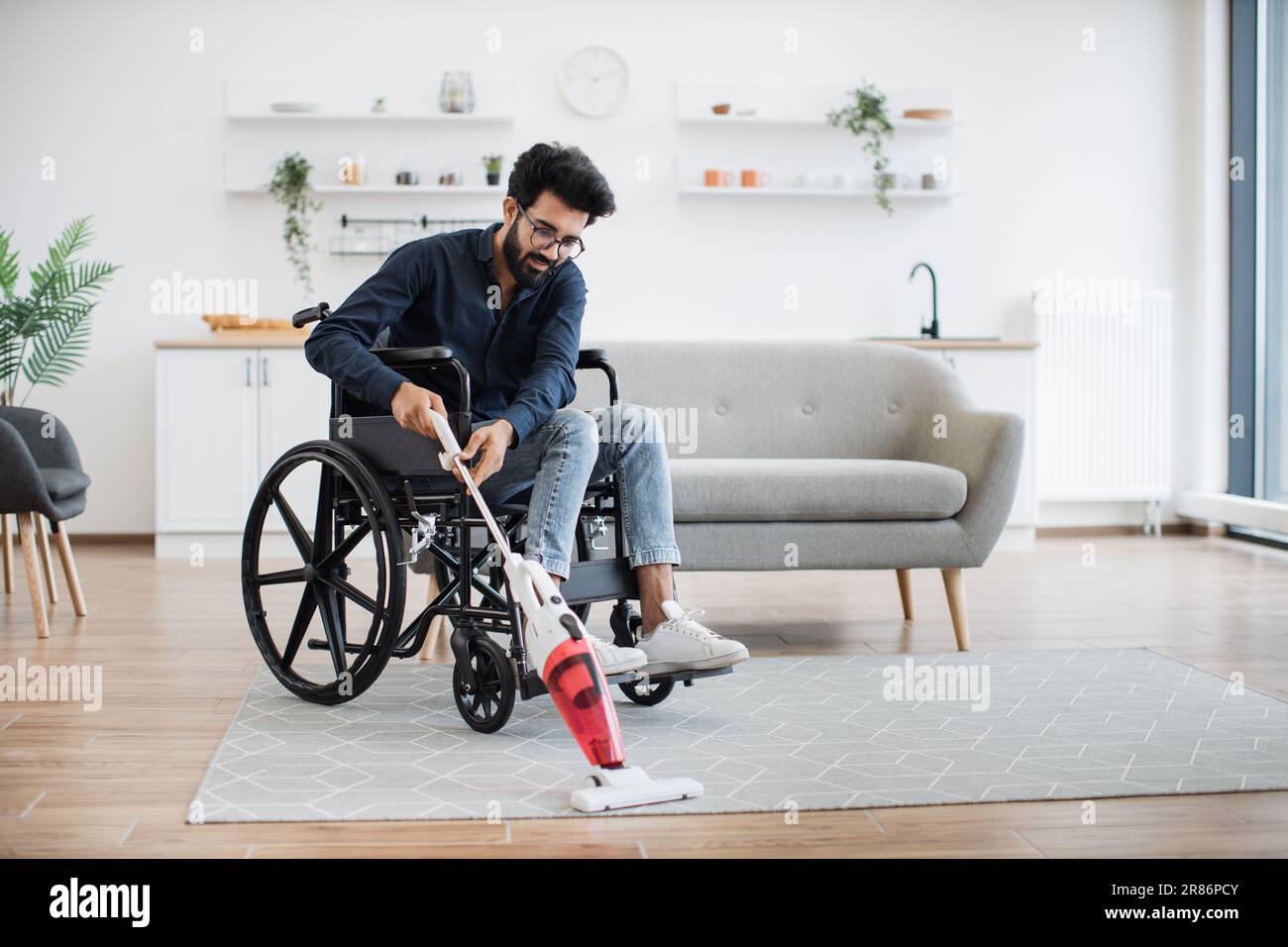 Helpful young man with disability holding cordless vacuum cleaner while