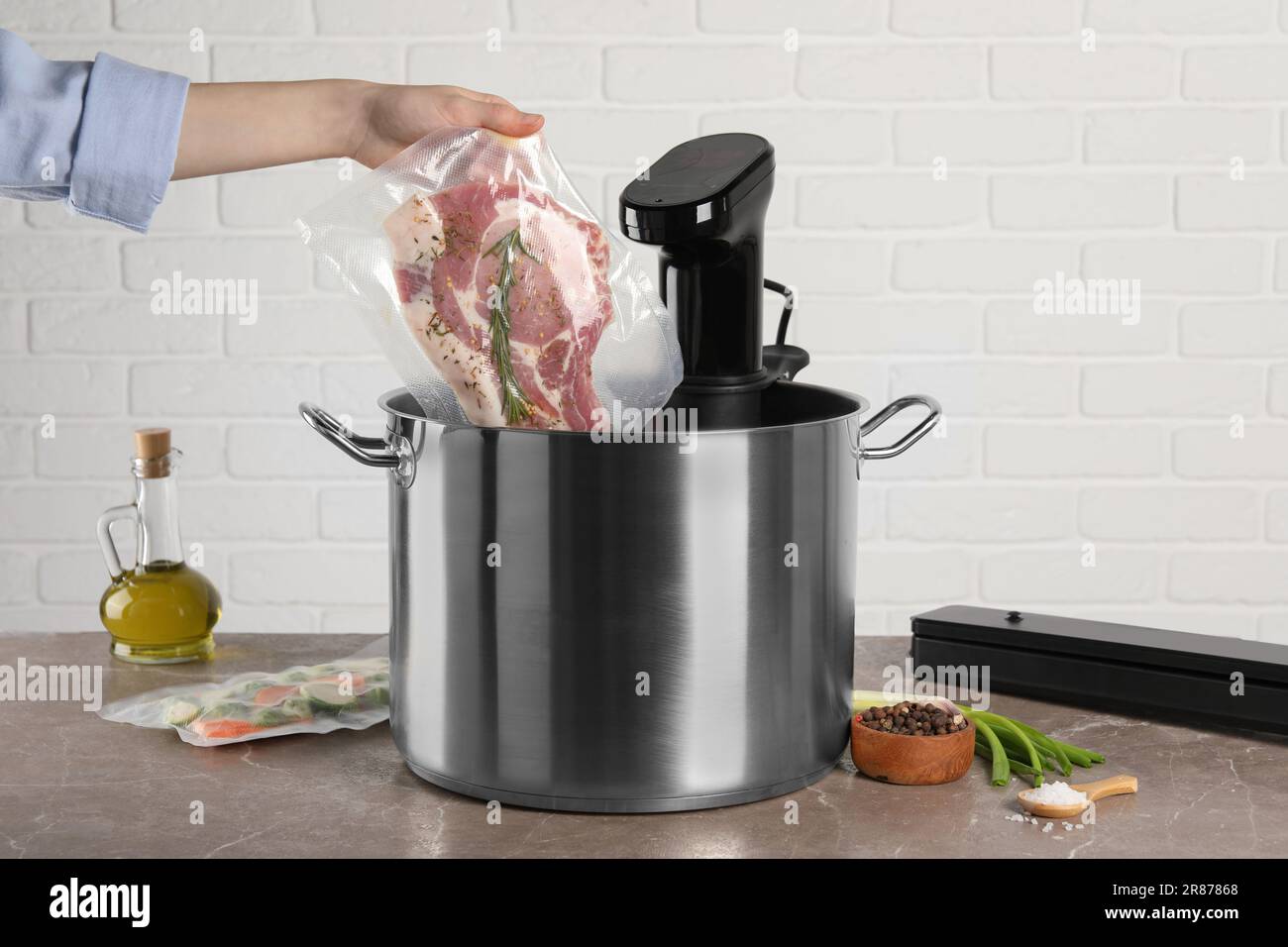 Woman putting vacuum packed meat into pot with sous vide cooker