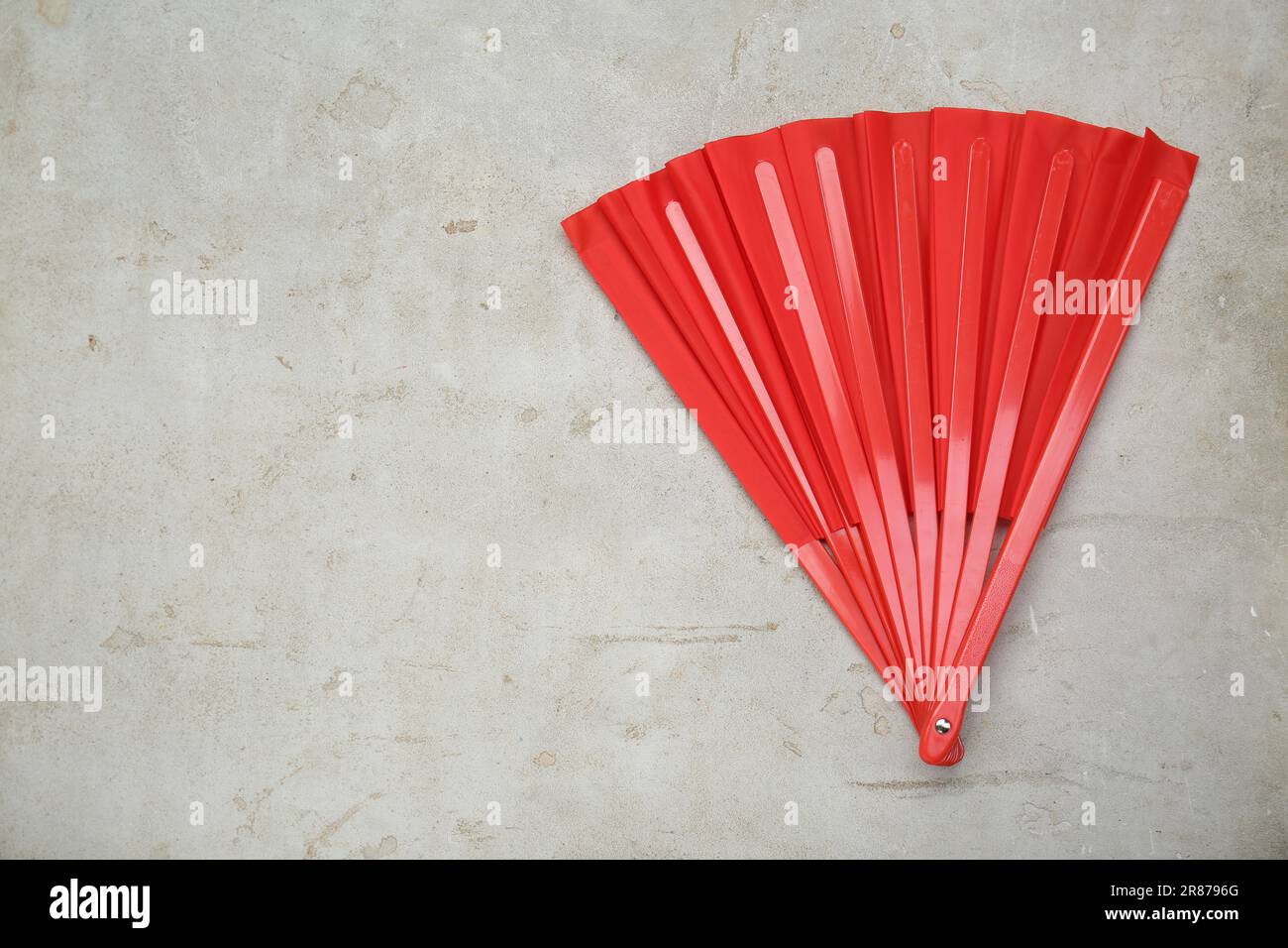 Bright red hand fan on old light grey background, top view. Space for