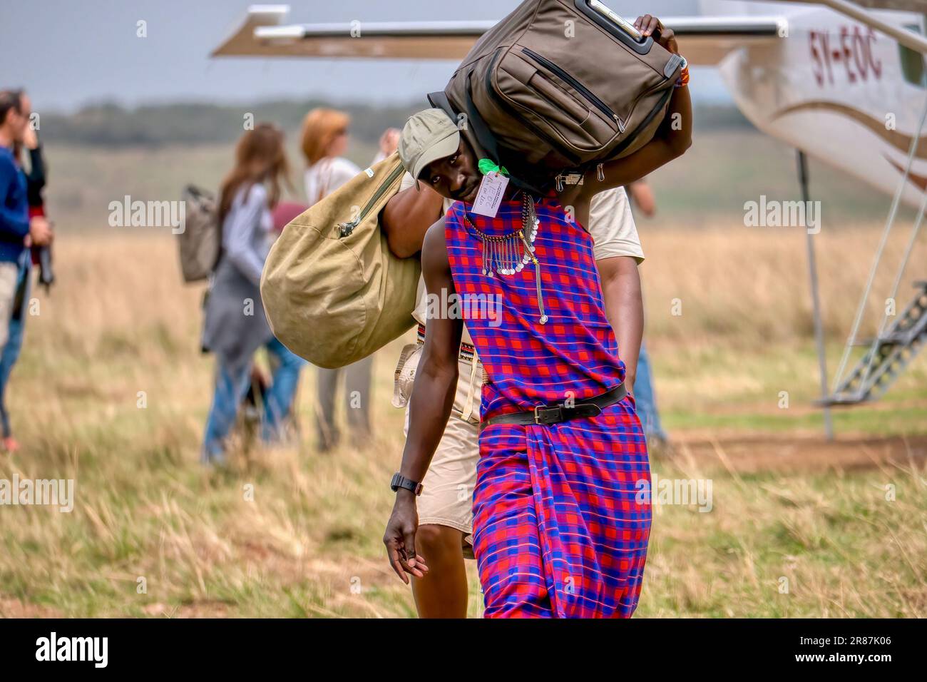 Maasai Mara, Kenya - September 25, 2013. A Maasai tribe member employed by a safari camp, carries passenger baggage from a charter flight. Stock Photo