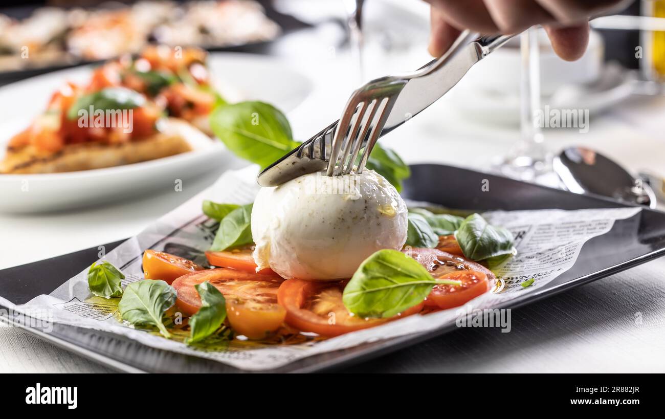 Cutlery used to cut into a ball of Mozzarella di Buffala on a Caprese style salad. Stock Photo