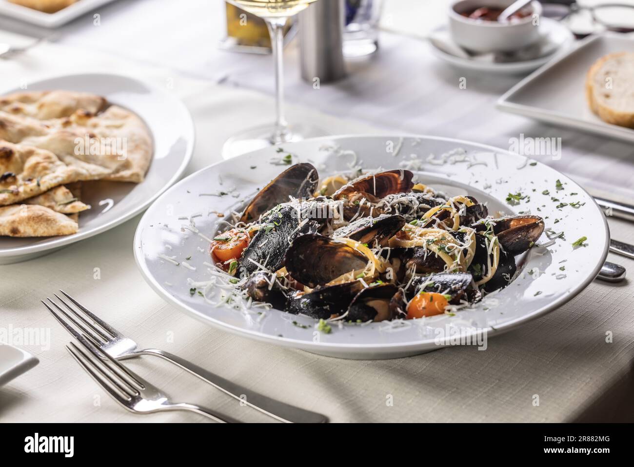 Linguine pasta with mussels and grated pecorino cheese on top served in a restaurant. Stock Photo