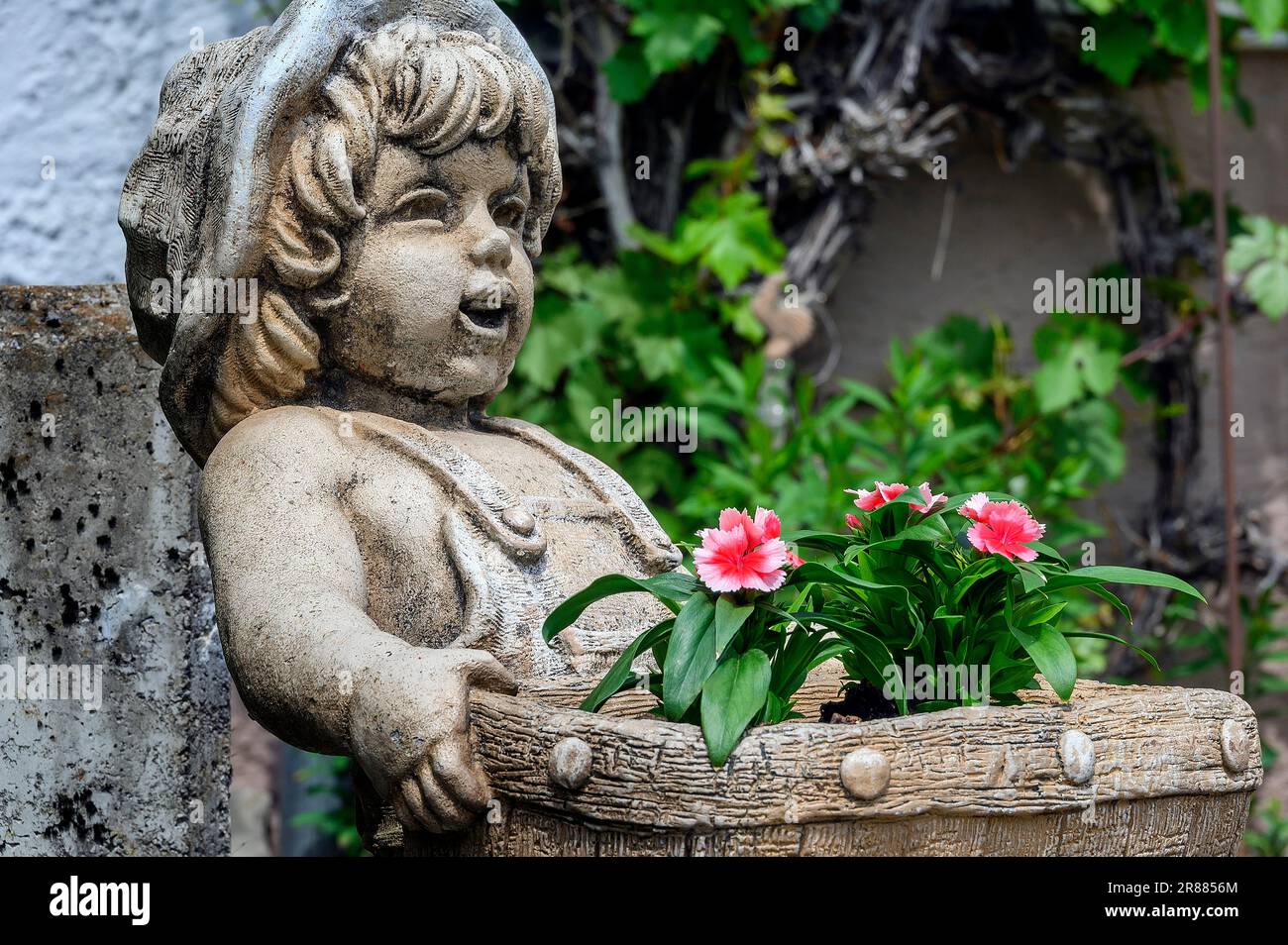 Childlike stone figure with flower basket and garden carnations, Allgaeu, Bavaria, Germany Stock Photo