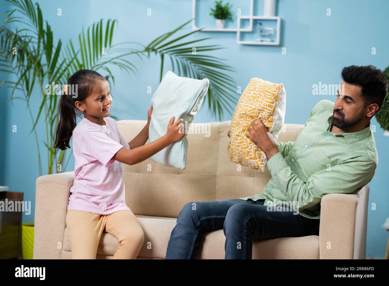 Happy Indian father with daughter playful fighting with pillow at home - concept of fatherhood, weekend playtime and family bonding Stock Photo