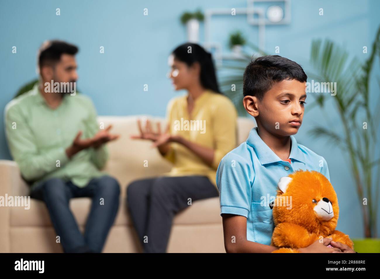 Indian sad kid with doll in front shouting and arguing couple at home - concept of family conflict, childhood trauma and emotional distress. Stock Photo