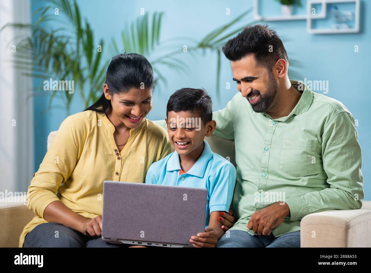 Indian couple got happy by seeing son using laptop while sitting together at home - concept of generation, family time and parenthood. Stock Photo