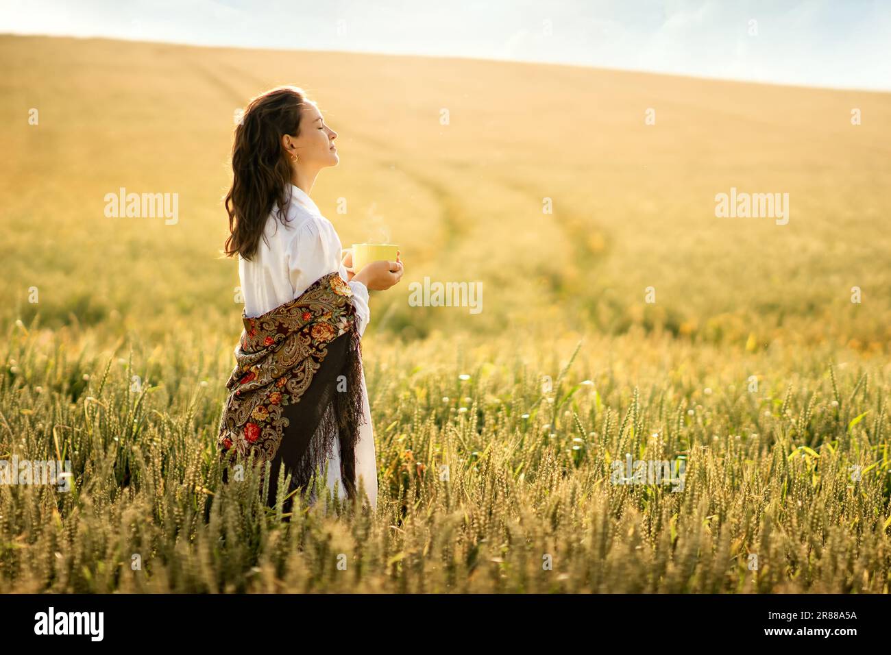 a young white woman went out at dawn to a wheat field to drink a cup of tea, coffee, to plunge into the atmosphere of tranquility, love, air, freedom. Stock Photo
