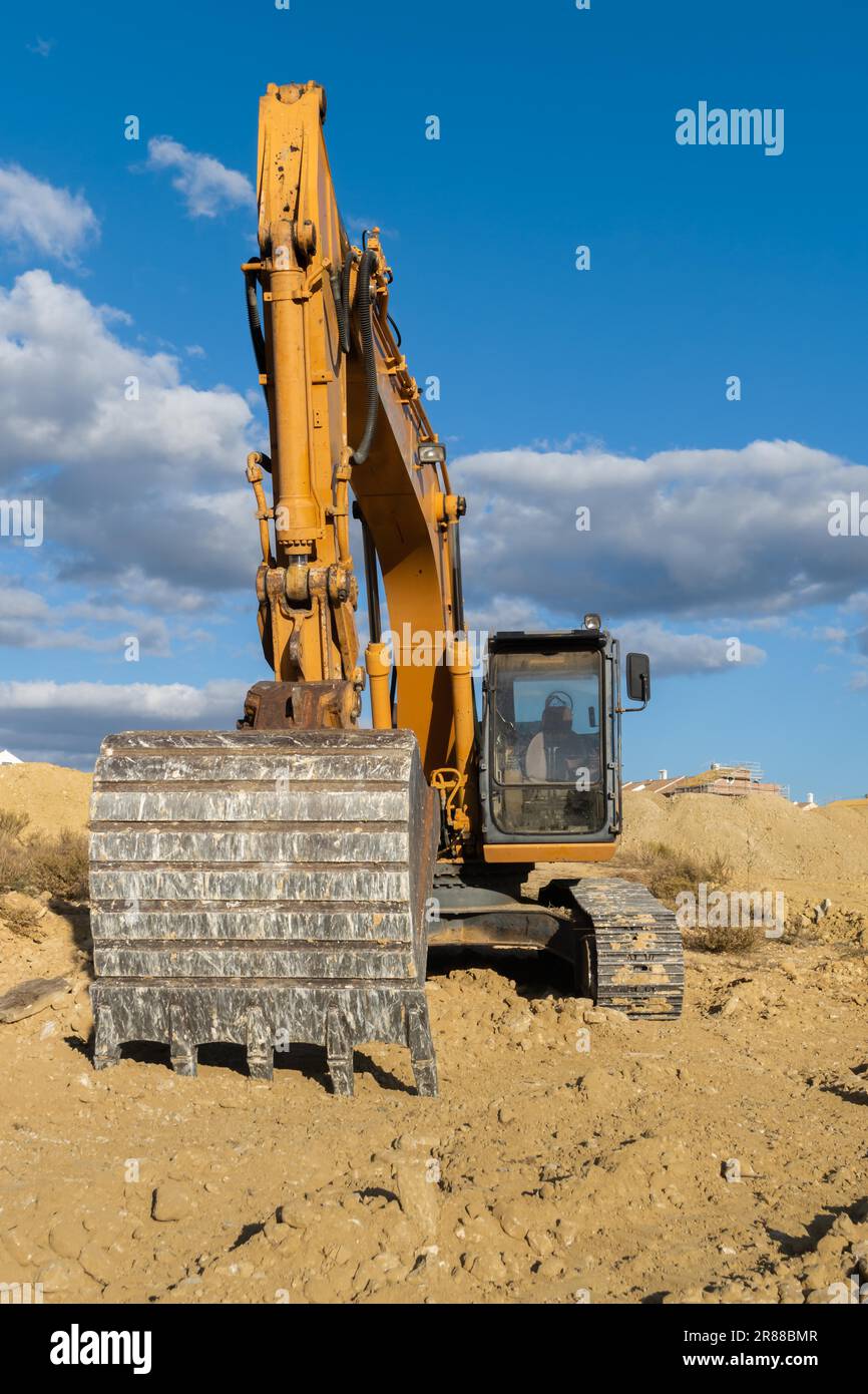 Large yellow excavator working on the construction site moving earth Stock Photo