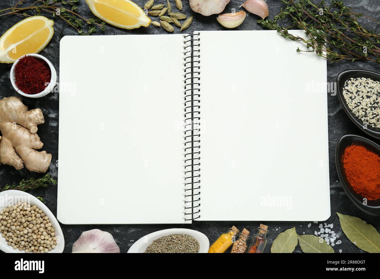 Blank recipe book surrounded by different ingredients on black textured table, flat lay. Space for text Stock Photo