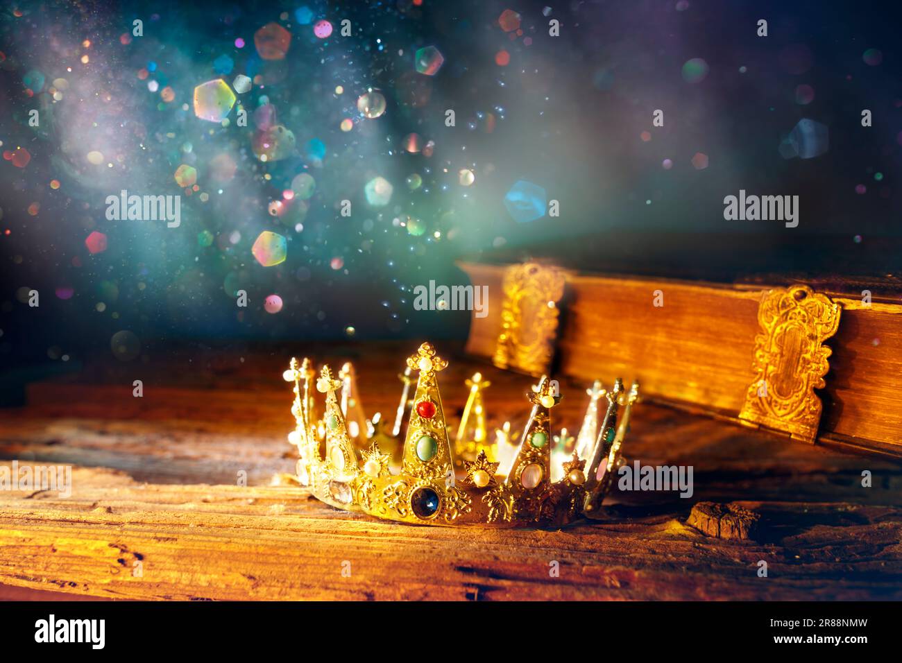 Medieval King Crown And Old Book - Story Of Fantasy kingdom With Magic Glittering And Abstract Defocused Lights Stock Photo