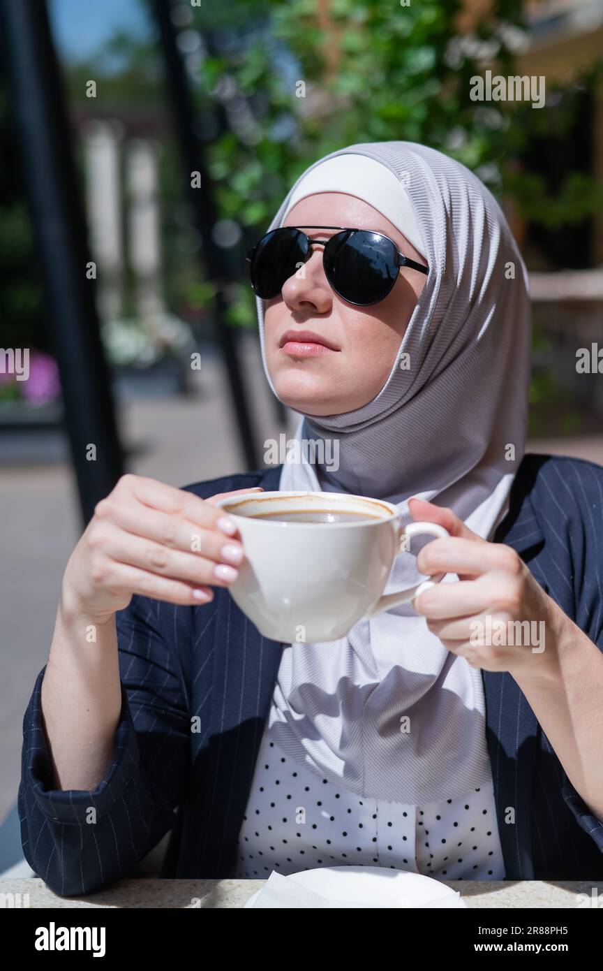 Caucasian woman in hijab drinking coffee in outdoor cafe Stock Photo ...