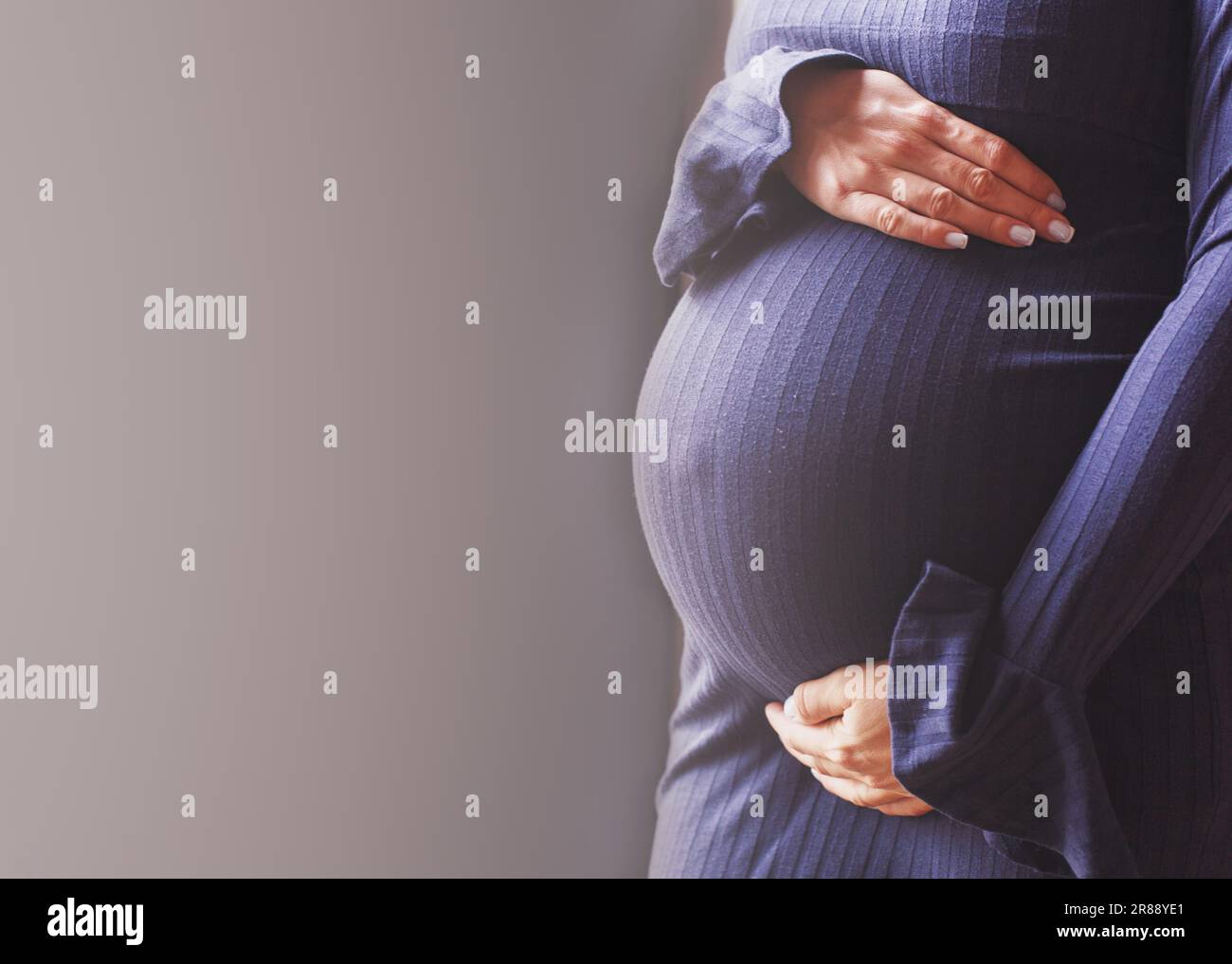 pregnant woman's belly closeup. Girls hands hugging her belly in blue background. Concept of maternal health. Stock Photo