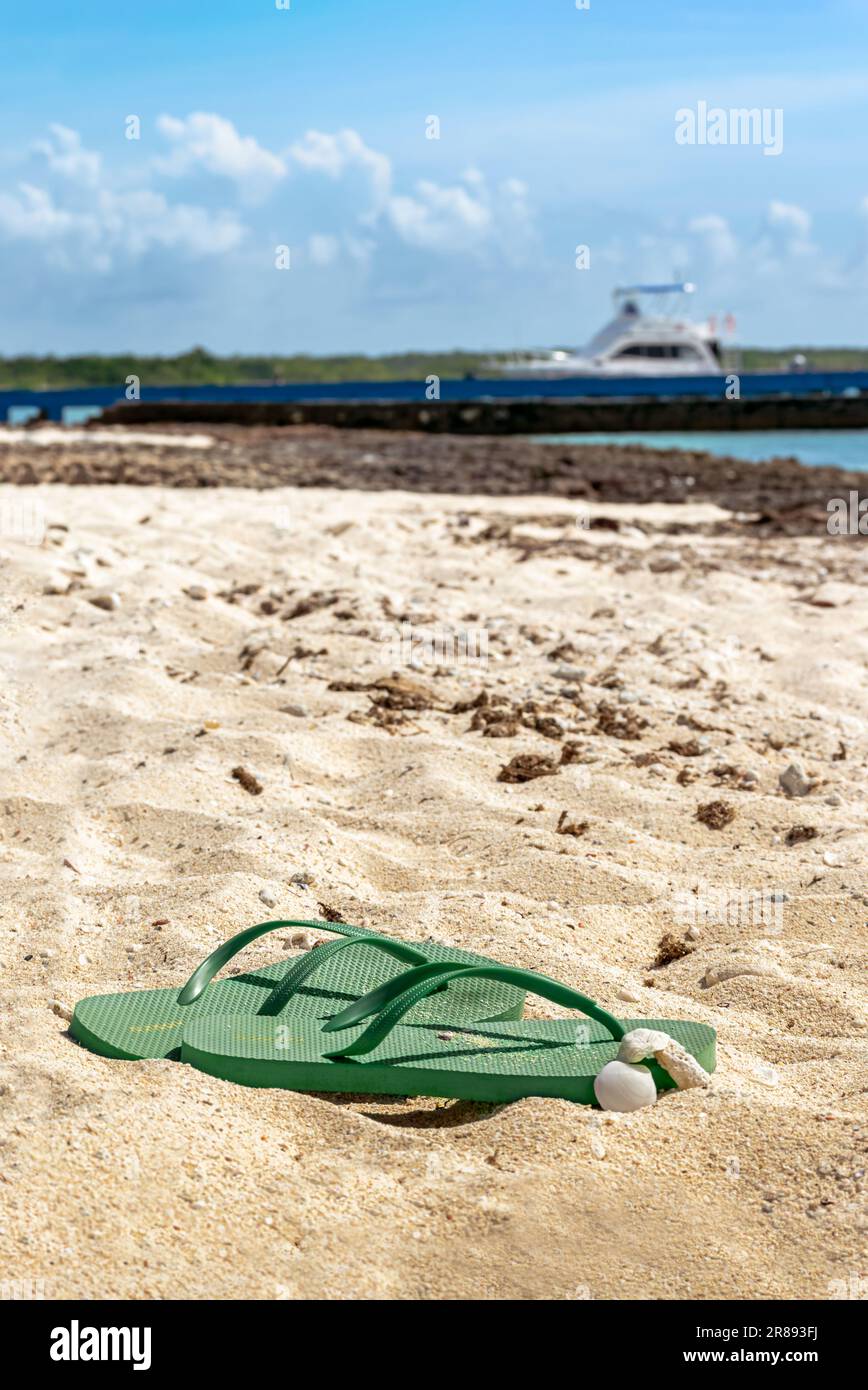 Close up photo of a pair of green flip-flops  on the sand of a Caribbean beach at daylight under the direct sunlight during summer time Stock Photo
