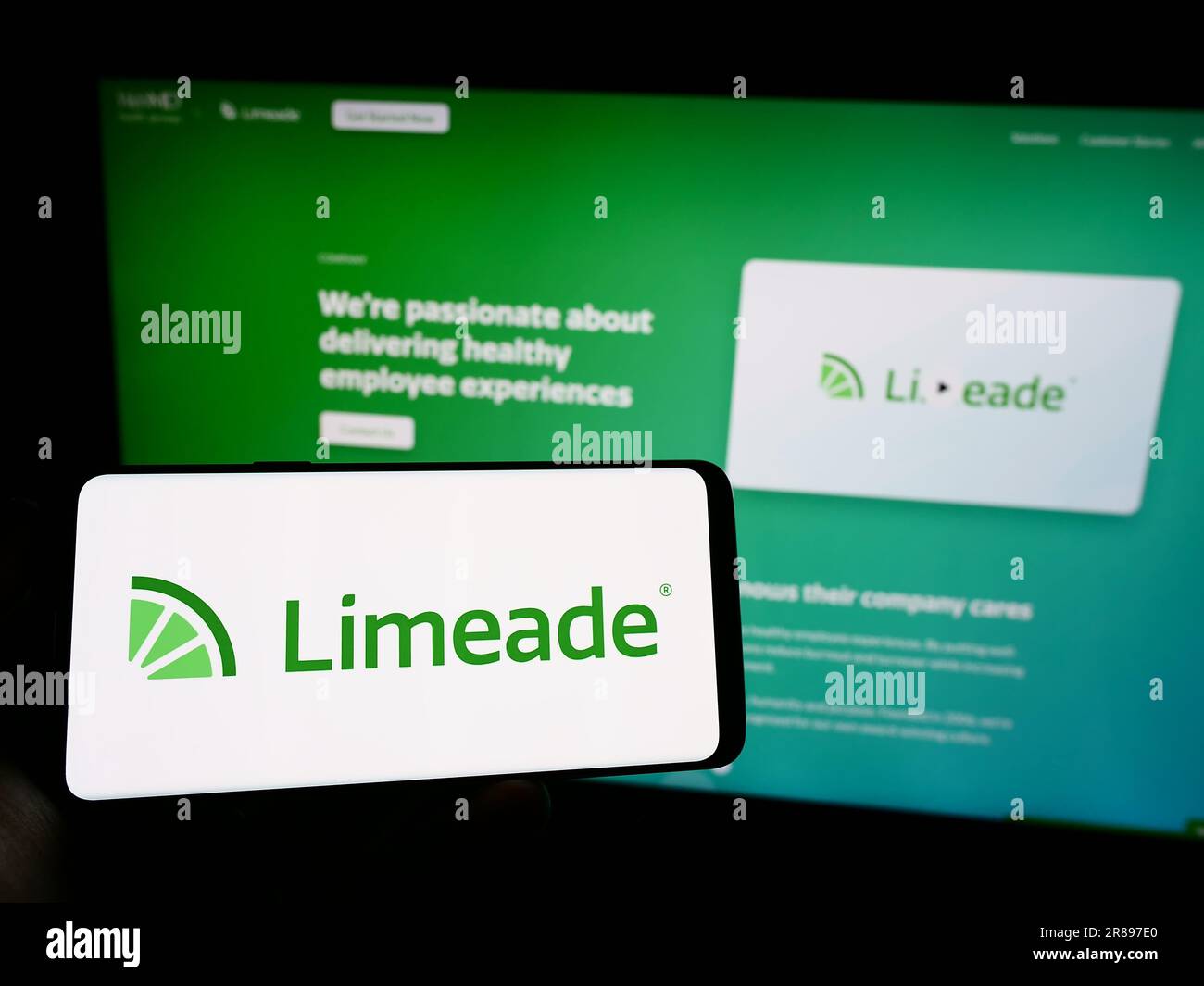 Person holding mobile phone with logo of American employee well-being company Limeade Inc. on screen in front of web page. Focus on phone display. Stock Photo