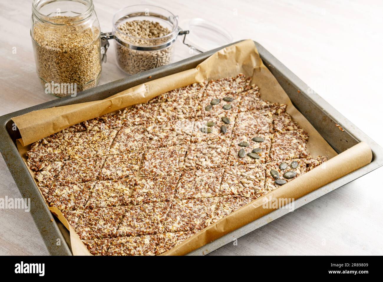 Baking tray with dough from linseed and oat flakes, cut into rhombs and topped with various seeds for healthy pastry snacks, copy space, selected focu Stock Photo