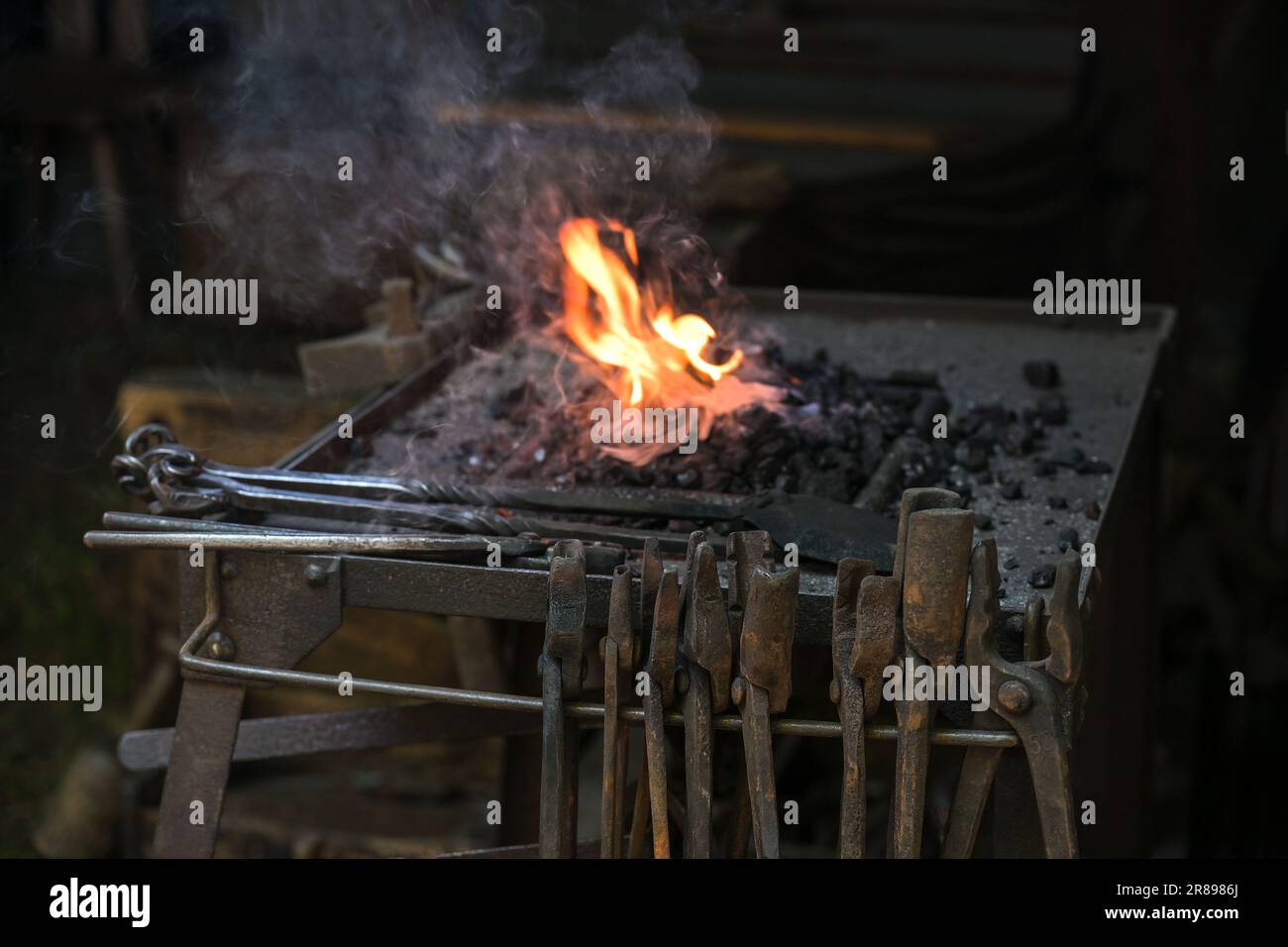 Portable forge of a blacksmith with various rusty tongs and a flaming coal fire at a historic craft market, copy space, selected focus, narrow depth o Stock Photo