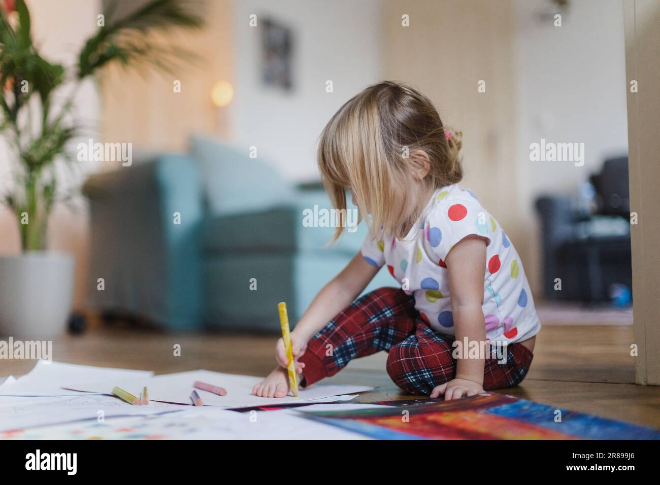 Cute little girl drawing with crayons, sitting on the floor at home. Stock Photo