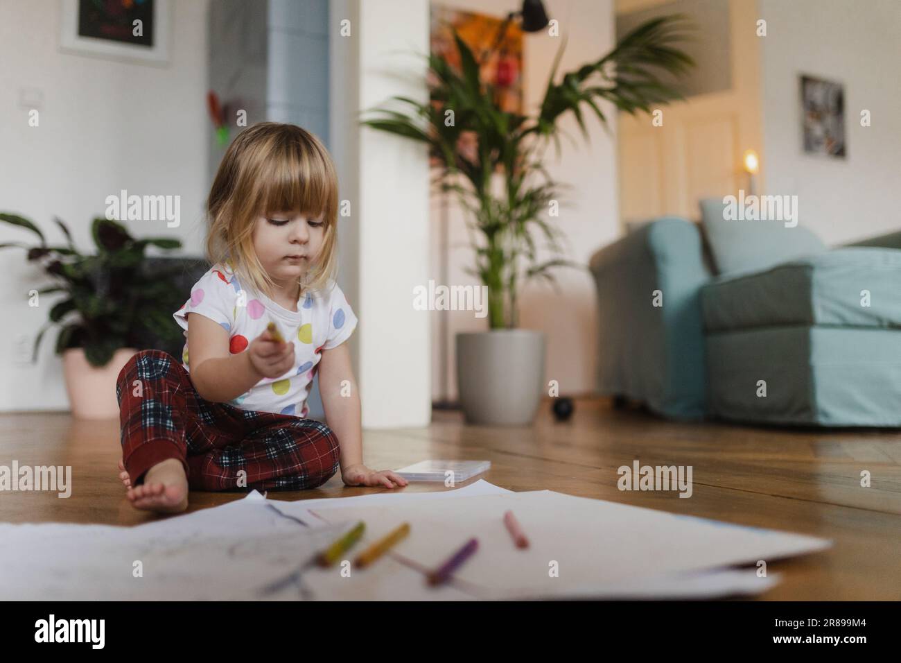 Cute little girl drawing with crayons, sitting on the floor at home. Stock Photo