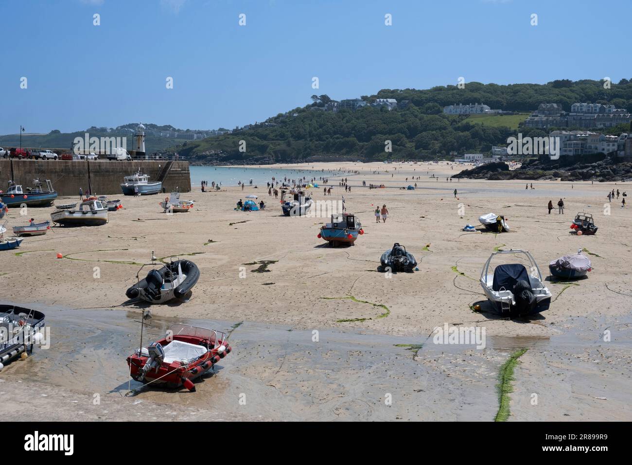 Holiday makers in the hot sunshine at the harbour of St Ives, Cornwall with the the tide out and the fishing boats resting on the sand. Stock Photo