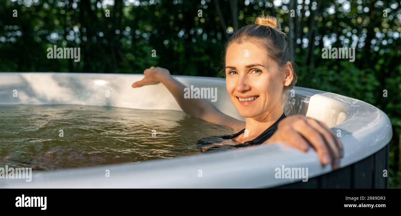 smiling young woman enjoying outdoor hot tub in forest. looking at camera. banner with copy space Stock Photo