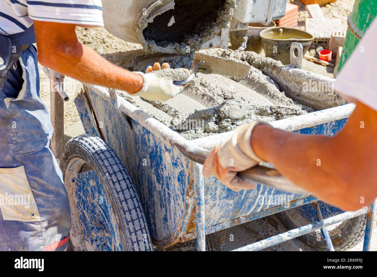 Teamwork, workers are pouring fresh mortar in wheelbarrow from mortar