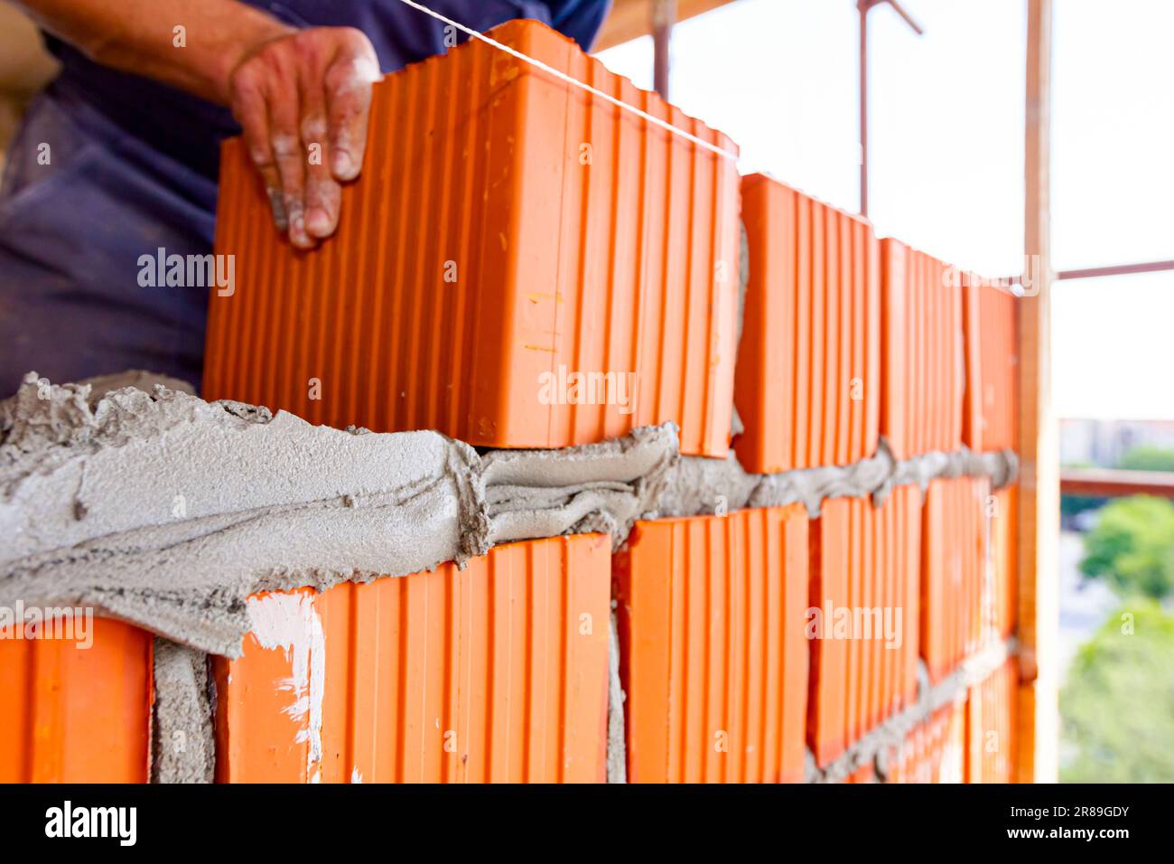 Mason, bricklayer worker is using red blocks to mount a wall next the