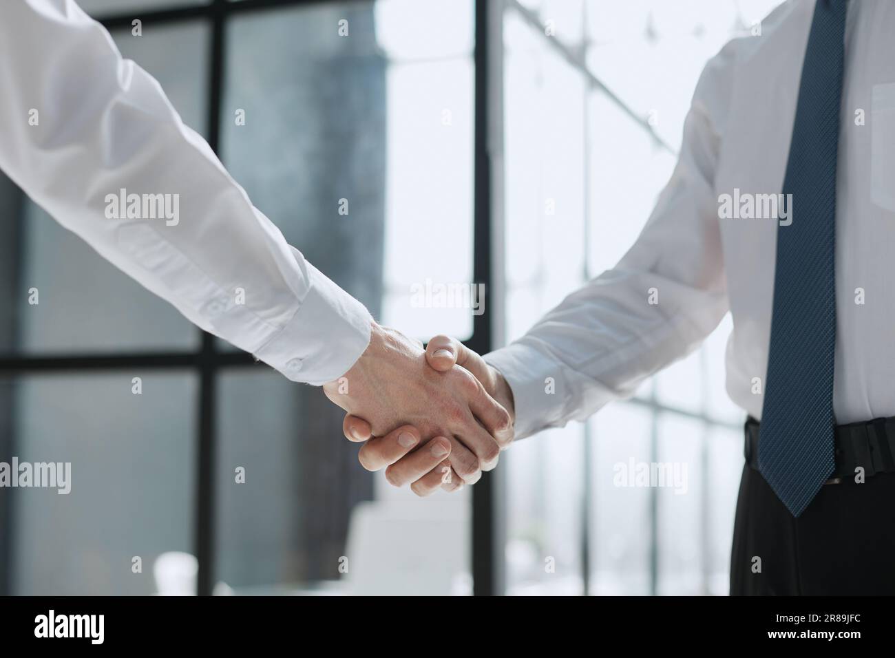 Two businessmen shake hands on the background of empty modern office, signing of a contract concept, close up Stock Photo