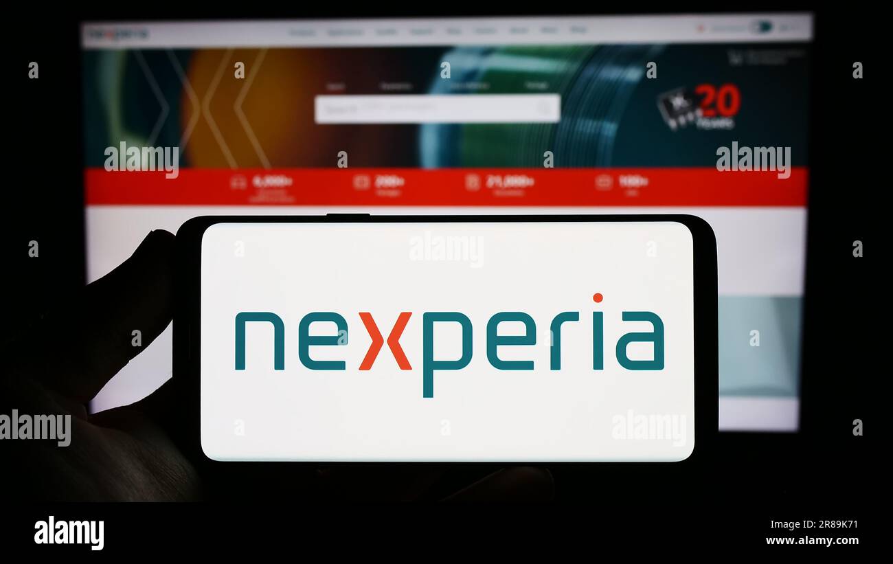 Person holding smartphone with logo of semiconductor company Nexperia B.V. on screen in front of website. Focus on phone display. Stock Photo