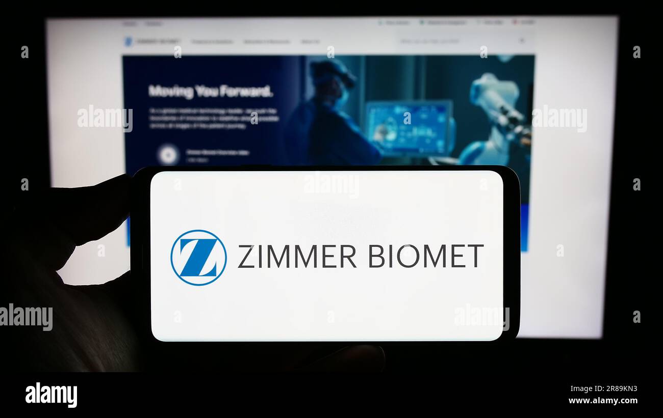 Person holding smartphone with logo of US company Zimmer Biomet Holdings Inc. on screen in front of website. Focus on phone display. Stock Photo