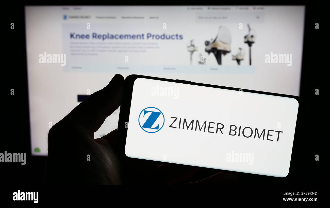 Person holding cellphone with logo of US company Zimmer Biomet Holdings Inc. on screen in front of business webpage. Focus on phone display. Stock Photo