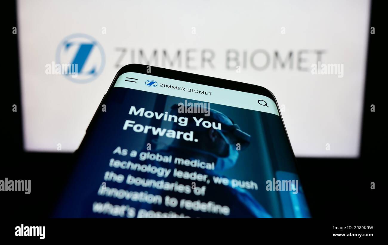 Mobile phone with website of US company Zimmer Biomet Holdings Inc. on screen in front of business logo. Focus on top-left of phone display. Stock Photo