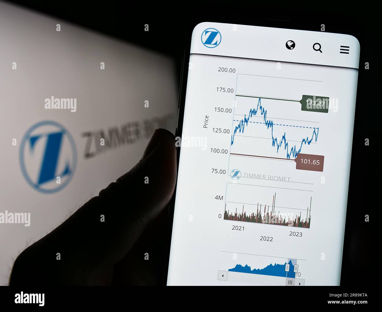 Person holding cellphone with webpage of US company Zimmer Biomet Holdings Inc. on screen in front of logo. Focus on center of phone display. Stock Photo
