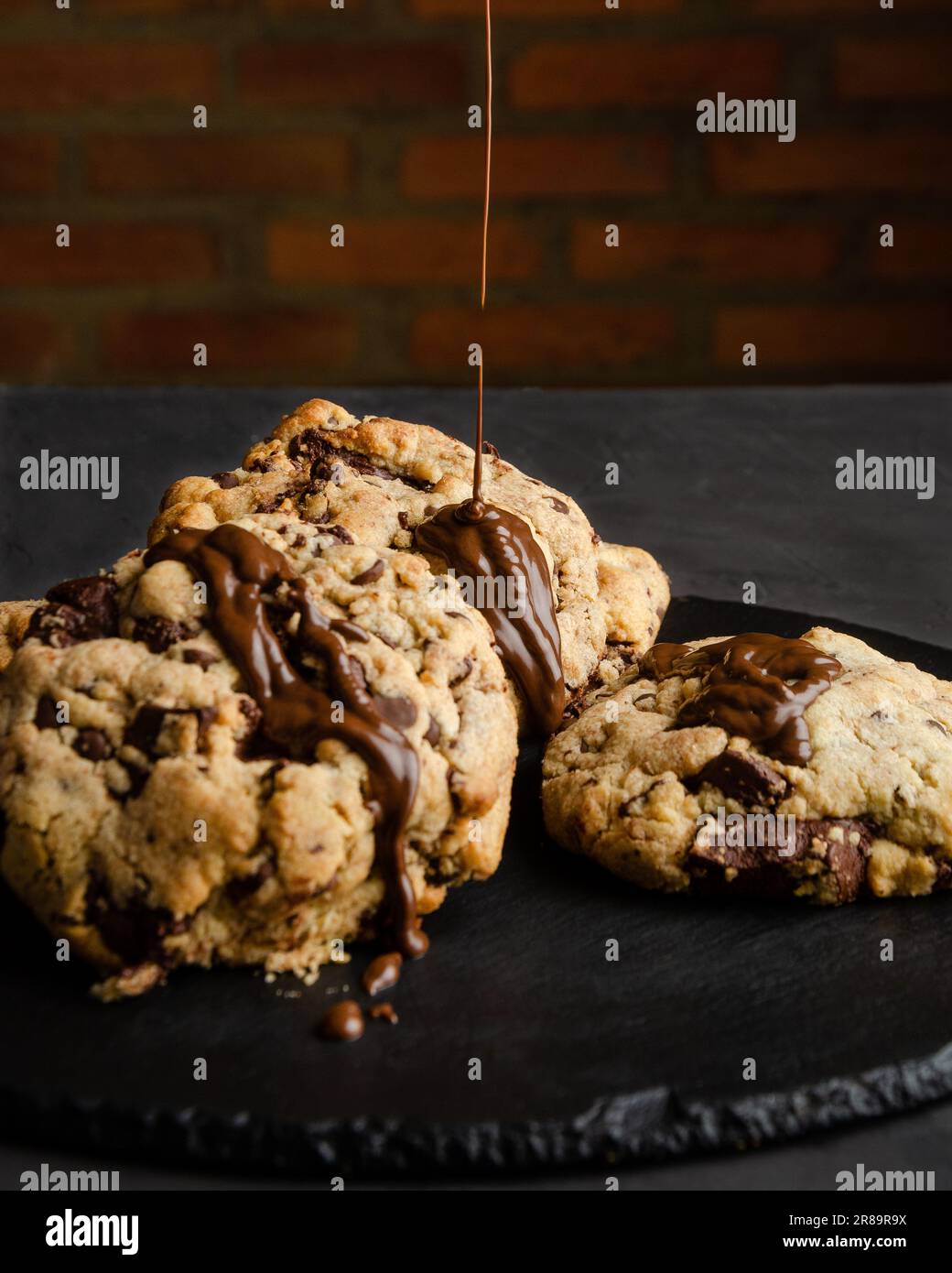 Chocolate chip cookies with chocolate syrup, on black background and brick wall Stock Photo