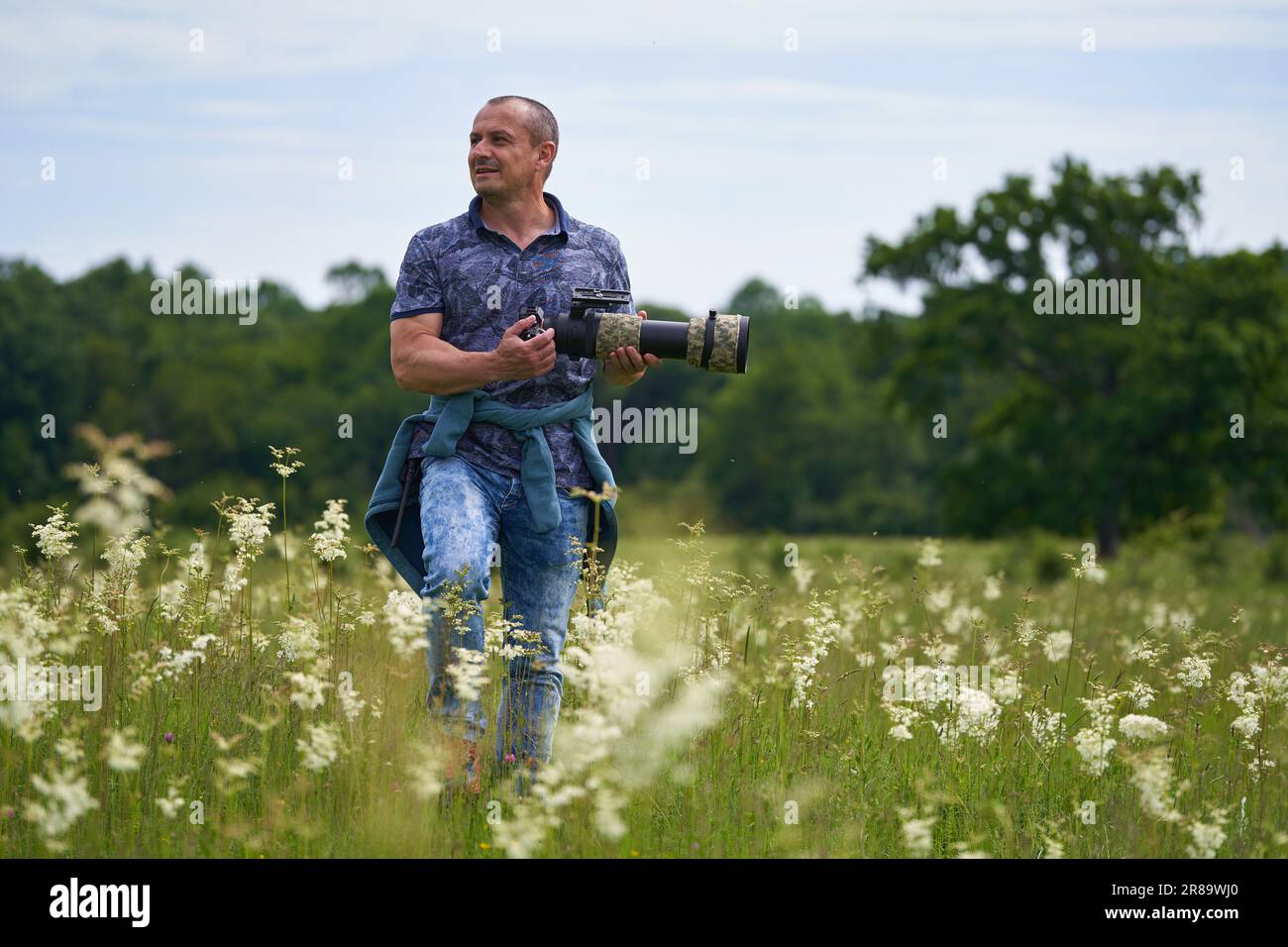 Professional nature photographer in the field by the forest, holding camera with a long telephoto lens Stock Photo