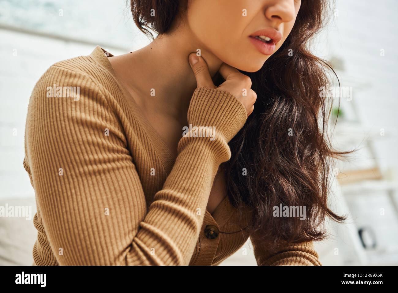 Cropped view of young brunette woman in brown jumper suffering from neck pain during self-massage at home, self-care ritual and holistic healing conce Stock Photo
