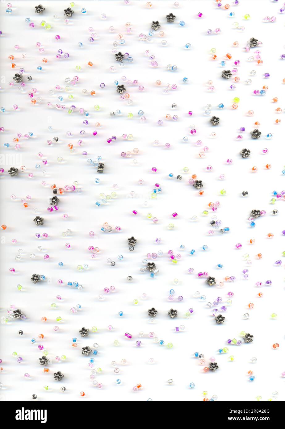 Colorful glass and flower beads scattered on a white background, top view. Craft supply for kids hobby of making jewelry - Stock Image