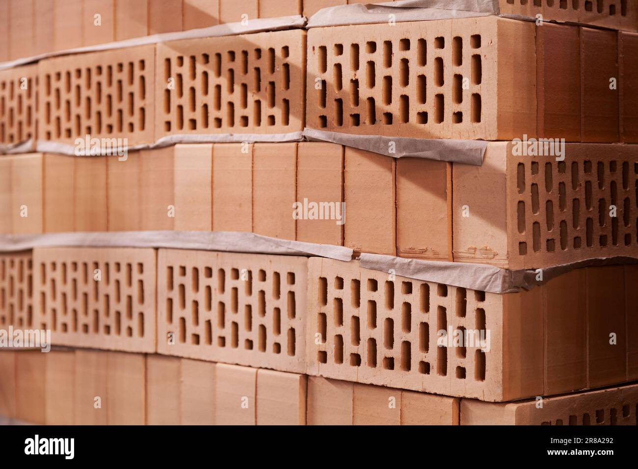 Many new hollow bricks stacked in a warehouse for sale. Lots of orange clay bricks at a construction site - Stock Image
