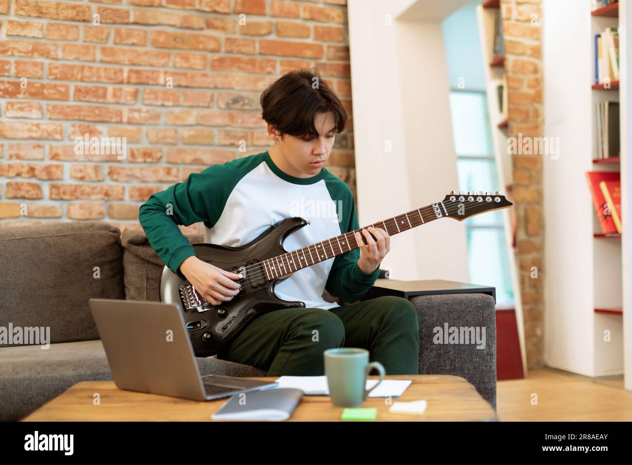 Japanese Teenager Boy Mastering Electric Guitar Chords Using Computer