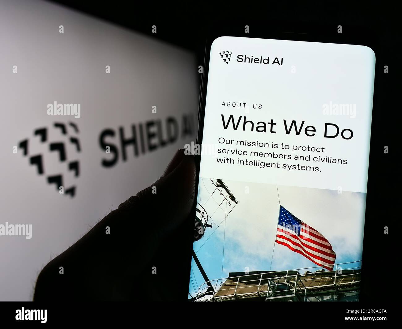 Person holding cellphone with webpage of US aerospace and defense company Shield AI on screen in front of logo. Focus on center of phone display. Stock Photo