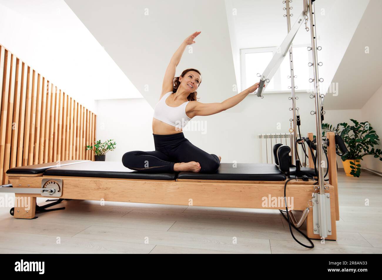 A woman is doing Pilates on a reformer bed in a bright studio. A