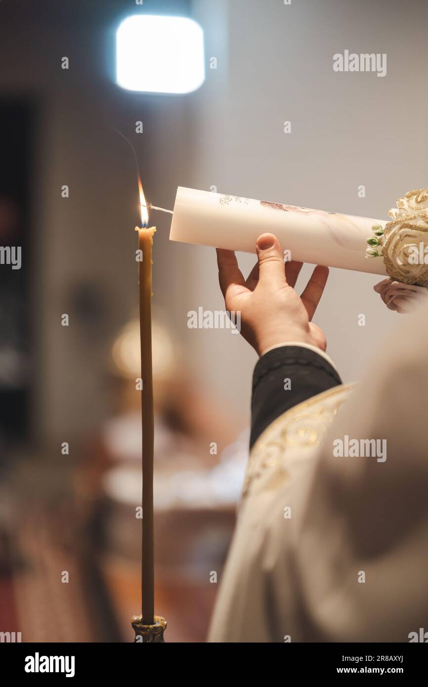 A person holding a lit candle in a decorative candleholder, using another candle as a source of fire in a religious setting Stock Photo