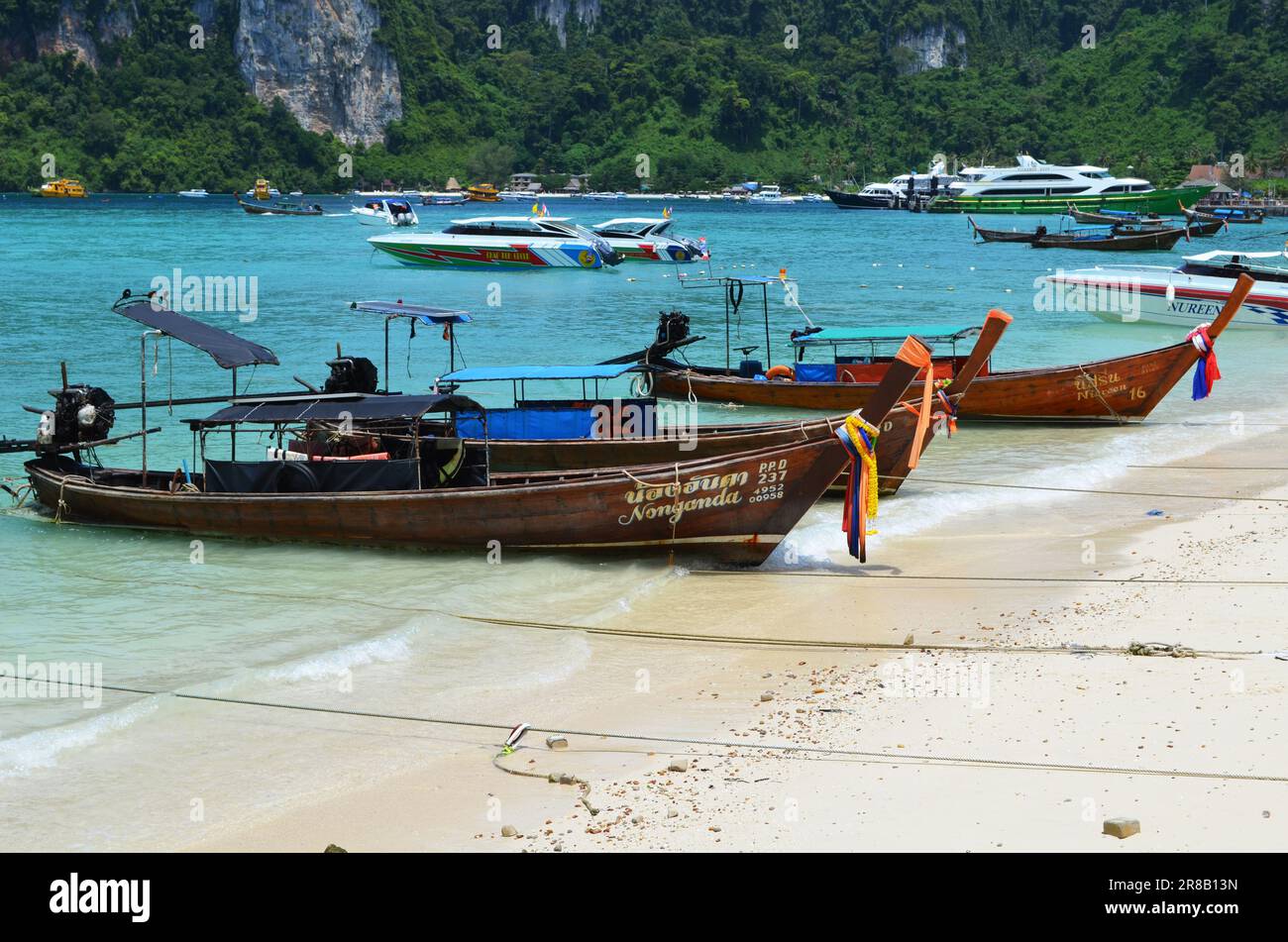 Two long-tail fishing boats on the beach of Phi Phi Island in Thailand, with sailing boats in the background. Stock Photo